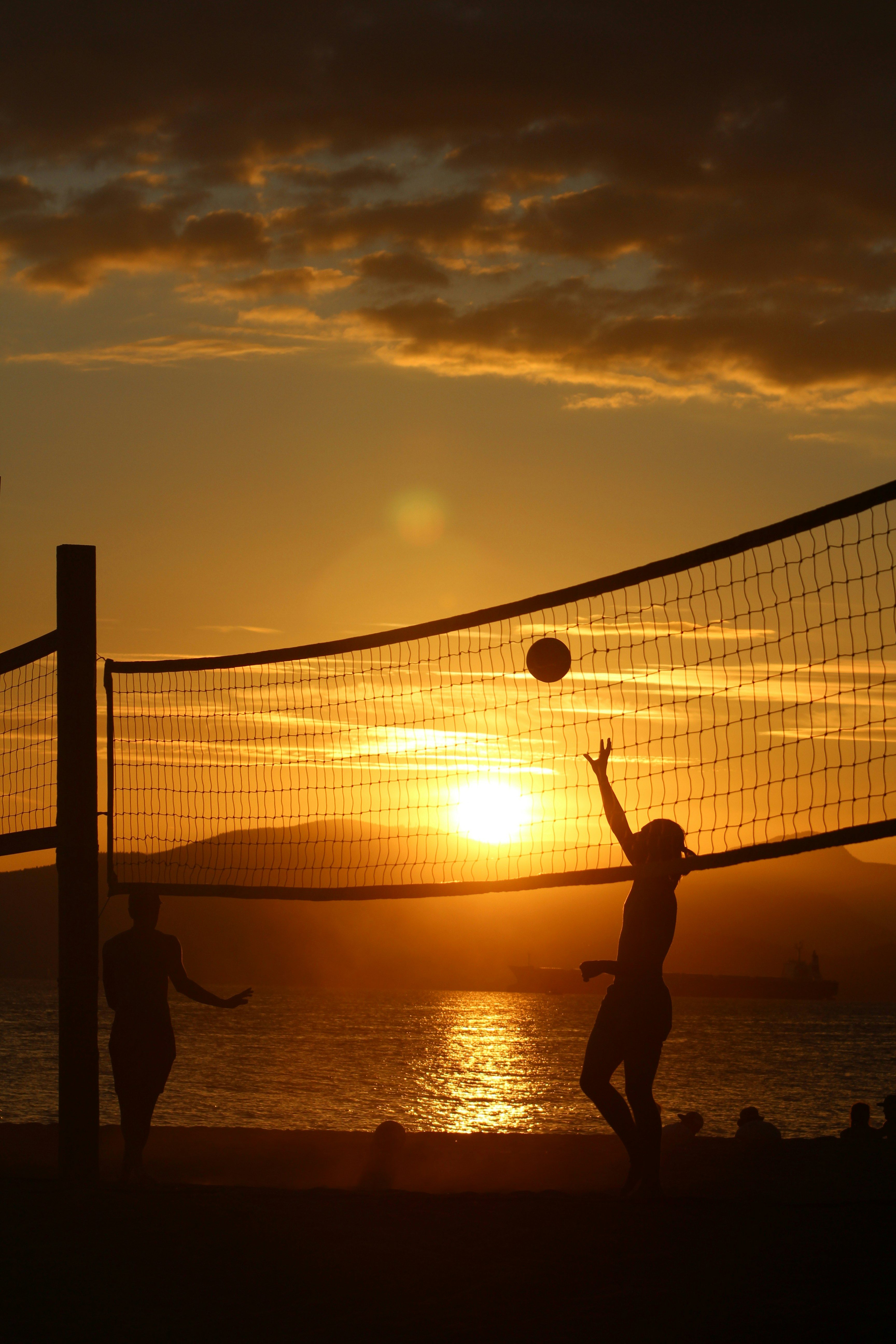 Players rallying on a beach volley court at golden hour.